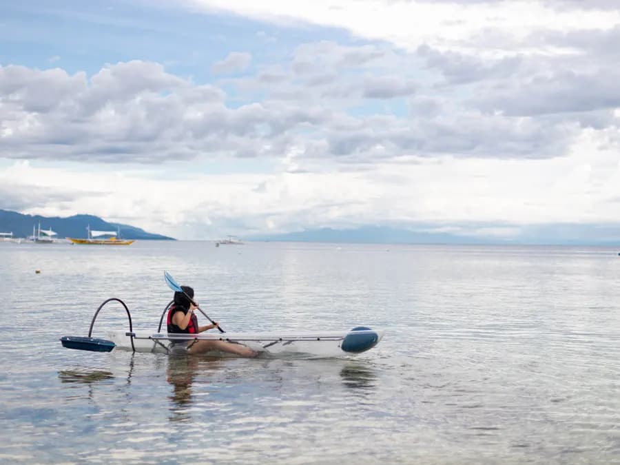 A guest paddling a clear kayak on calm open water off the beach